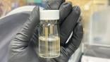 gloved hand holding a vial of battery electrolyte