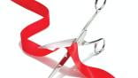 Pair of scissors cutting red ribbon