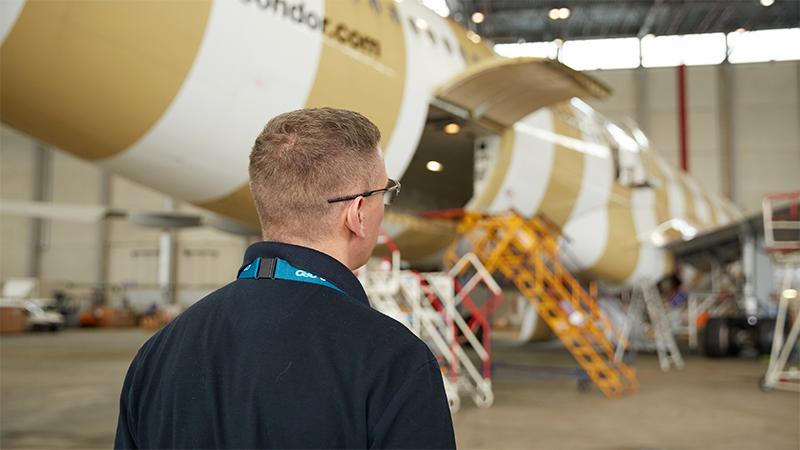 Rear view of person standing by Condor aircraft in hangar