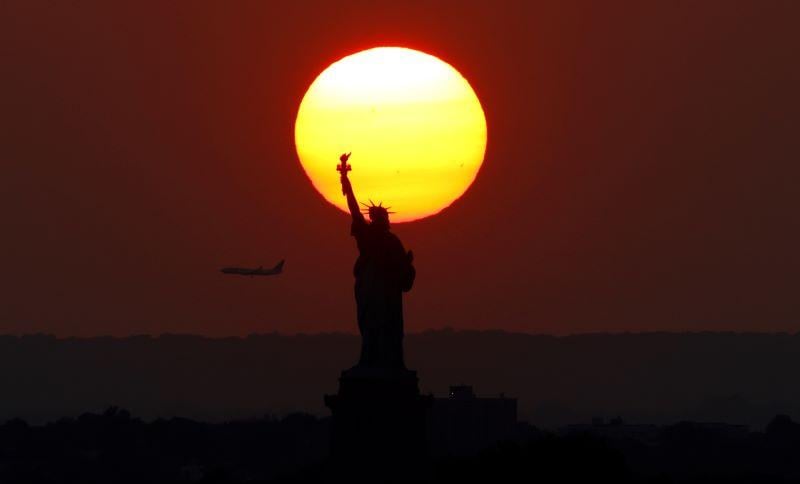 sunset behind the statue of liberty with an airplane in the sky