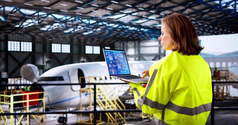 a woman working on a laptop standing in front of an aircraft